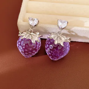 Gros plan détaillé de boucles d'oreilles fraises en résine violette avec clous en cristal cœur
