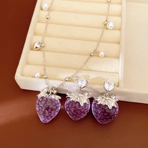 Vue détaillée d'un ensemble de bijoux fraise en résine violette et perles blanches.
