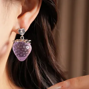 Gros plan d'une boucle d'oreille fraise en résine violette avec cristal en forme de cœur.