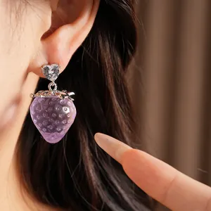 Gros plan d'une jolie boucle d'oreille fraise en résine violette avec un cœur
