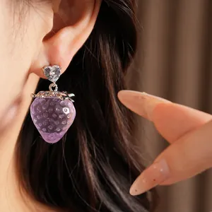Gros plan d'une boucle d'oreille fraise en résine violette avec cristal en forme de cœur.