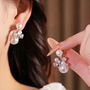 Elegant zirconia and pearl ear clips for women, shown on ear and held by hand.