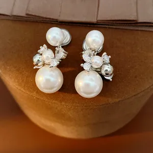 Detailed view of elegant pearl and zircon clip-on earrings on a brown velvet stand.
