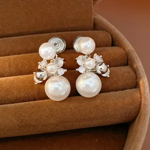 Detailed close-up of elegant pearl and zircon ear clips in a brown velvet jewelry box.