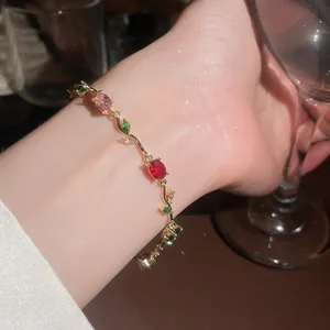 Detailed view of a gold vine bracelet with red and green gemstones on a wrist