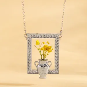 Dettaglio del ciondolo a cornice argentata con fiori secchi gialli e rilievo vaso