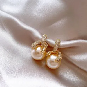 Dettaglio di eleganti orecchini placcati oro con pavé di zirconi e perle champagne