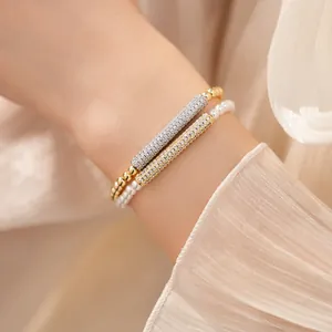 Close-up of elegant gold and pearl beaded bracelets with zircon-encrusted cylinder charms