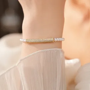 Close-up detail of a pavé zircon gold bar and white pearl bracelet on a wrist.