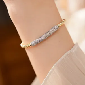 Macro view of exquisite zirconia-paved bamboo bar on elegant gold beaded bracelet