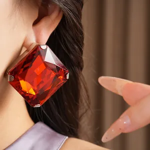 Macro detail shot showing a vibrant large red square crystal stud earring on model's ear