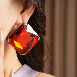 Detailed macro view of large red square rhinestone stud earrings worn by an elegant model