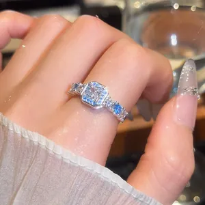 Detailed view of luxury square zircon ring with blue accent stones on a female hand.