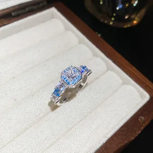 Close-up detail of a silver-finish ring with square zircon and blue stones in a jewelry box.