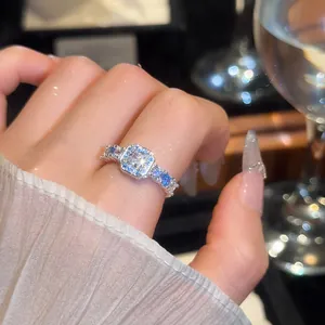 Close-up of a luxury square zircon ring with blue side stones on a finger