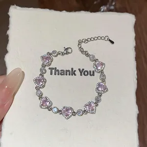 Gros plan d'un bracelet en argent avec des zircons roses en forme de cœur sur une carte cadeau.