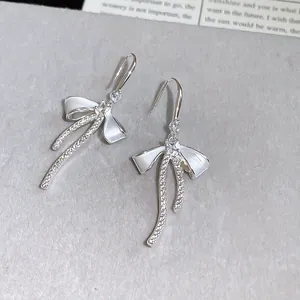 Close-up of elegant bowknot earrings with sparkling zircons and white enamel finish