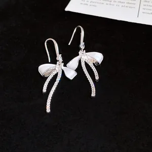 Detailed macro view of sparkling zircon bow-knot ear hooks featuring elegant white enamel finish