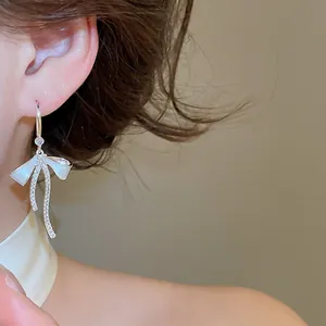 Detailed shot of elegant bow earrings with sparkling zircons and white enamel