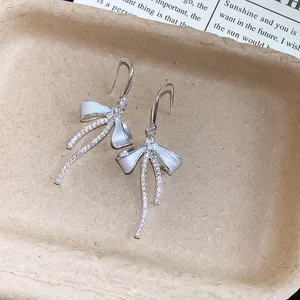 Close-up of sparkling zircon bow earrings with white enamel finish on a neutral tray.