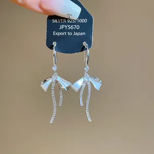 Detailed macro view of silver bow earrings with zircons and white enamel finish.