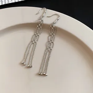 Close-up of elegant silver tassel earrings with zircon studs on a beige plate
