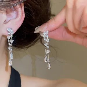 Dettaglio di orecchini a clip con nappe, zirconi a cuore e goccia sull'orecchio.