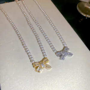 Close-up of zircon bowknot pendant pearl necklaces in gold and silver finishes.
