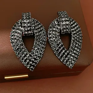 Primo piano di orecchini neri a forma di foglia con strass su una scatola di gioielli.