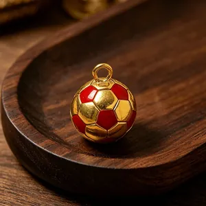Detailaufnahme eines 18k vergoldeten Fußballanhängers mit roter Emaille auf Holztablett.