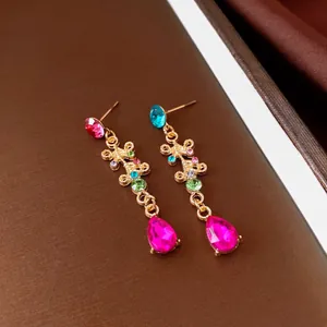 Dettaglio di orecchini pendenti vintage con strass colorati e goccia rosa brillante.