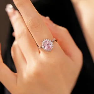 Silver-toned ring featuring an oval pink zircon with a halo of clear stones on a hand