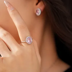 Close-up of elegant pink oval zircon ring and matching halo earrings on model.