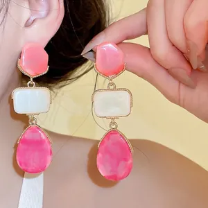 Pendientes largos de resina estilo dopamina con formas geométricas rosas y blancas en dorado.