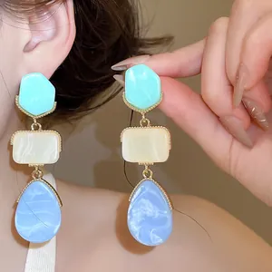 Primer plano detallado de pendientes de resina con colgantes de gota de agua azules.