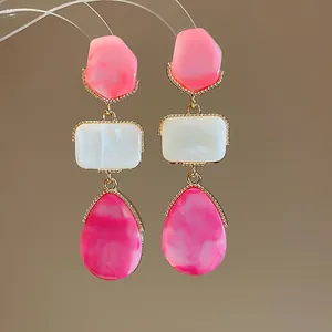 Detalle de pendientes de resina dopamina con colgantes geométricos en rosa y blanco.