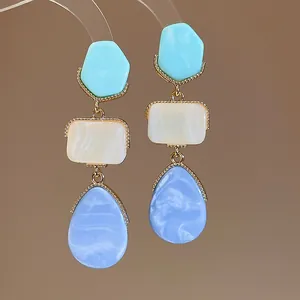 Primer plano de pendientes de resina con hermosas texturas jaspeadas en azul y crema