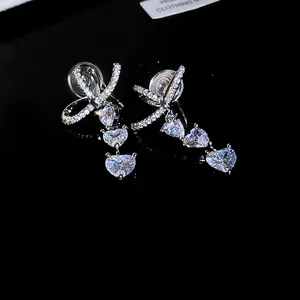 Close-up of elegant silver-toned bowknot drop earrings with three heart zircons