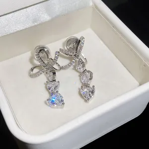Close-up of sparkling cubic zirconia bow and heart drop clip-on earrings in a white box
