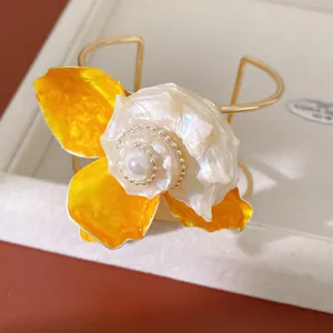 Primer plano de un brazalete dorado con una gran flor amarilla y centro de nácar natural.