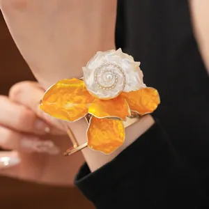Primer plano detallado de un brazalete audaz con concha y flor naranja en la muñeca de una mujer