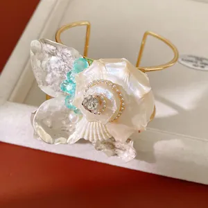 Vista detallada de un brazalete de flor de concha con pedrería y cuentas brillantes.