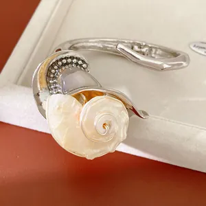 Primer plano del detalle de concha y perla en una elegante pulsera de brazalete plateado