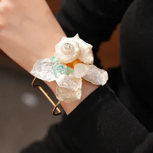 Primer plano de un brazalete de flor de concha exagerado con pedrería y piedras turquesas.