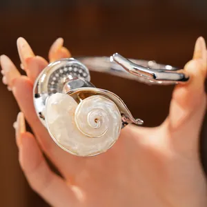Vista detallada de un brazalete de plata con una gran concha en espiral de estilo de lujo.