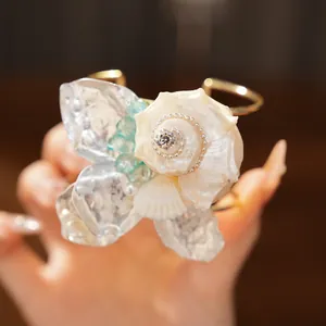 Primer plano de un lujoso brazalete dorado con una gran flor de concha y brillantes diamantes