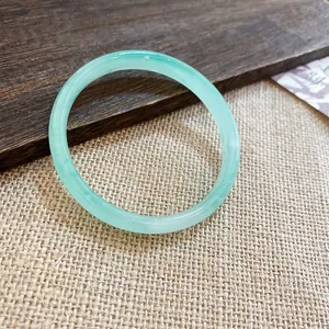 Dettaglio ravvicinato di un bracciale in calcedonia verde chiaro su superficie in lino