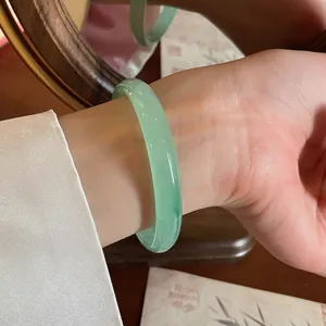 Dettaglio ravvicinato di un bracciale tondo in calcedonio verde traslucido al polso.