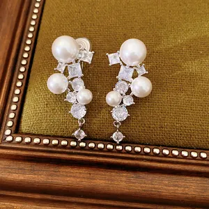 Close-up detail of geometric zircon and pearl ear clips on vintage green fabric