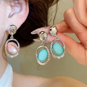 Close-up detail of silver-tone oval earrings featuring pink and blue acrylic pendants.